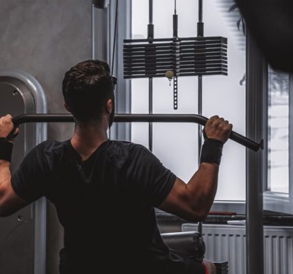 Back view of a man exercising with lat pulldown machine in the gym.