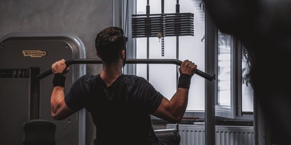 Back view of a man exercising with lat pulldown machine in the gym.